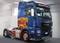 Un camion bleu avec un design de flammes distinctif sur le côté est stationné dans un hall. L'inscription 'Grampan G. Dodino' est visible en haut.