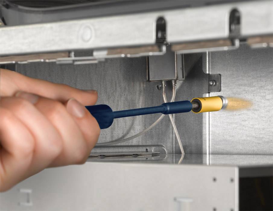 Une main tient un outil bleu et jaune et remplace une bougie d'allumage dans une cuisinière à gaz.