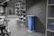 Grand espace de stockage moderne aux murs gris. Des étagères remplies de boîtes bleues. Une poubelle avec un sac bleu est placée contre le mur.