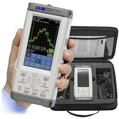 Une main tient un analyseur de spectre RF portable avec un écran affichant des données de mesure. En arrière-plan, un étui ouvert contenant des accessoires.