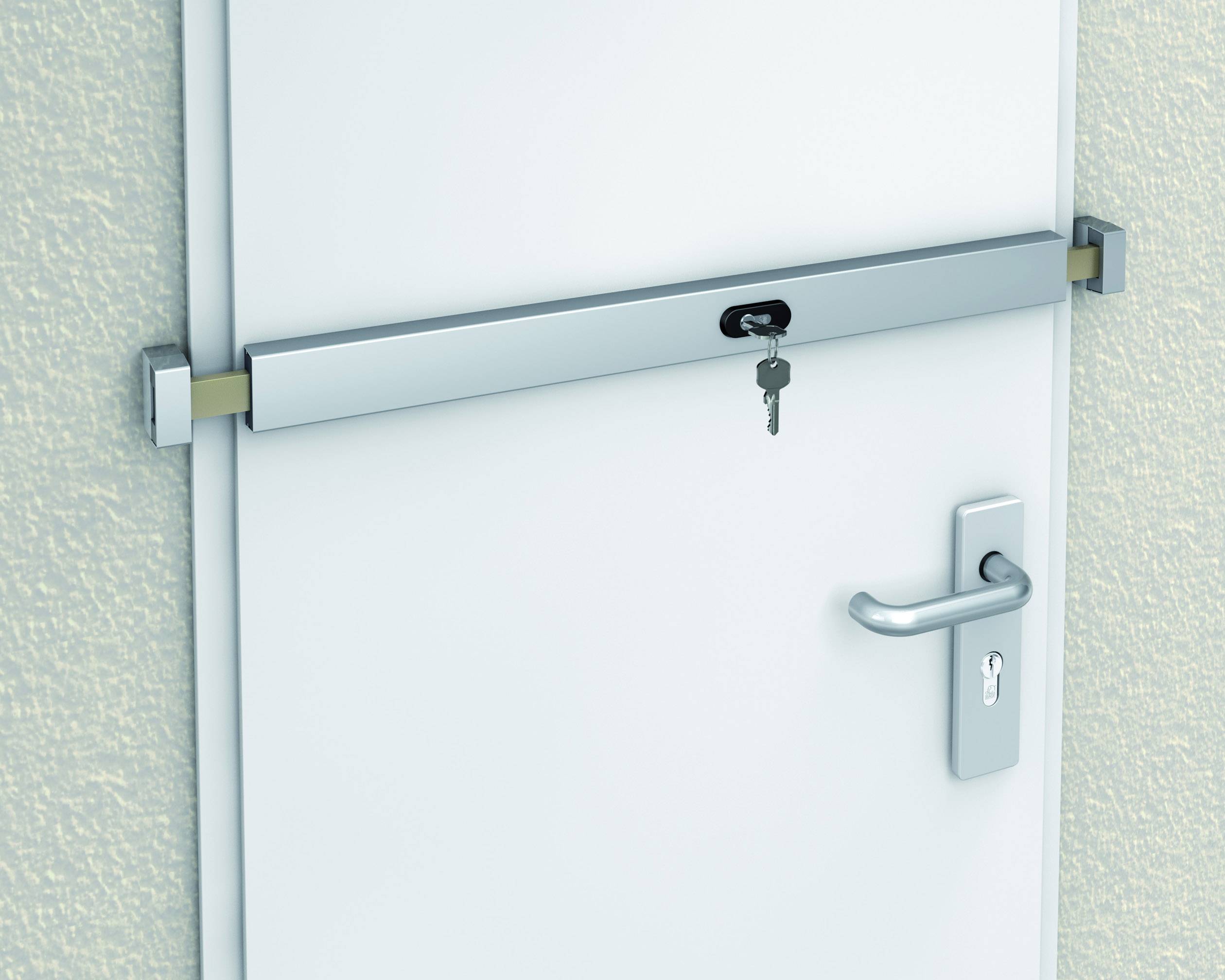 Barre de sécurité argentée sur une porte blanche avec une clé dans la serrure. La poignée de porte se trouve à droite.