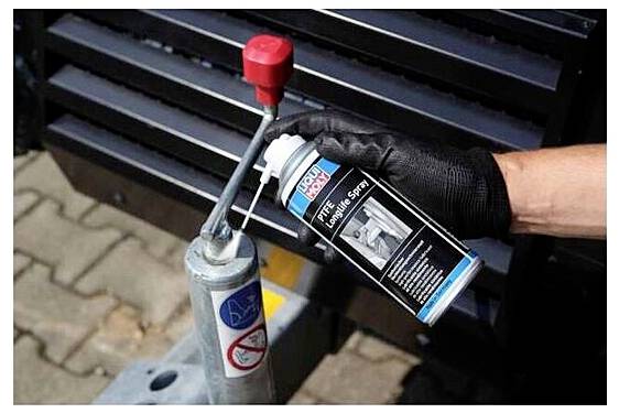 'Une personne portant un gant noir applique un spray PTFE longue durée sur la zone d'accouplement de la machinerie, améliorant la lubrification et réduisant les frottements.'