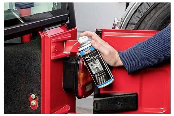 Une personne vaporise du lubrifiant sur la charnière de la porte de voiture rouge à des fins d'entretien, assurant un fonctionnement régulier et prévenant la rouille.