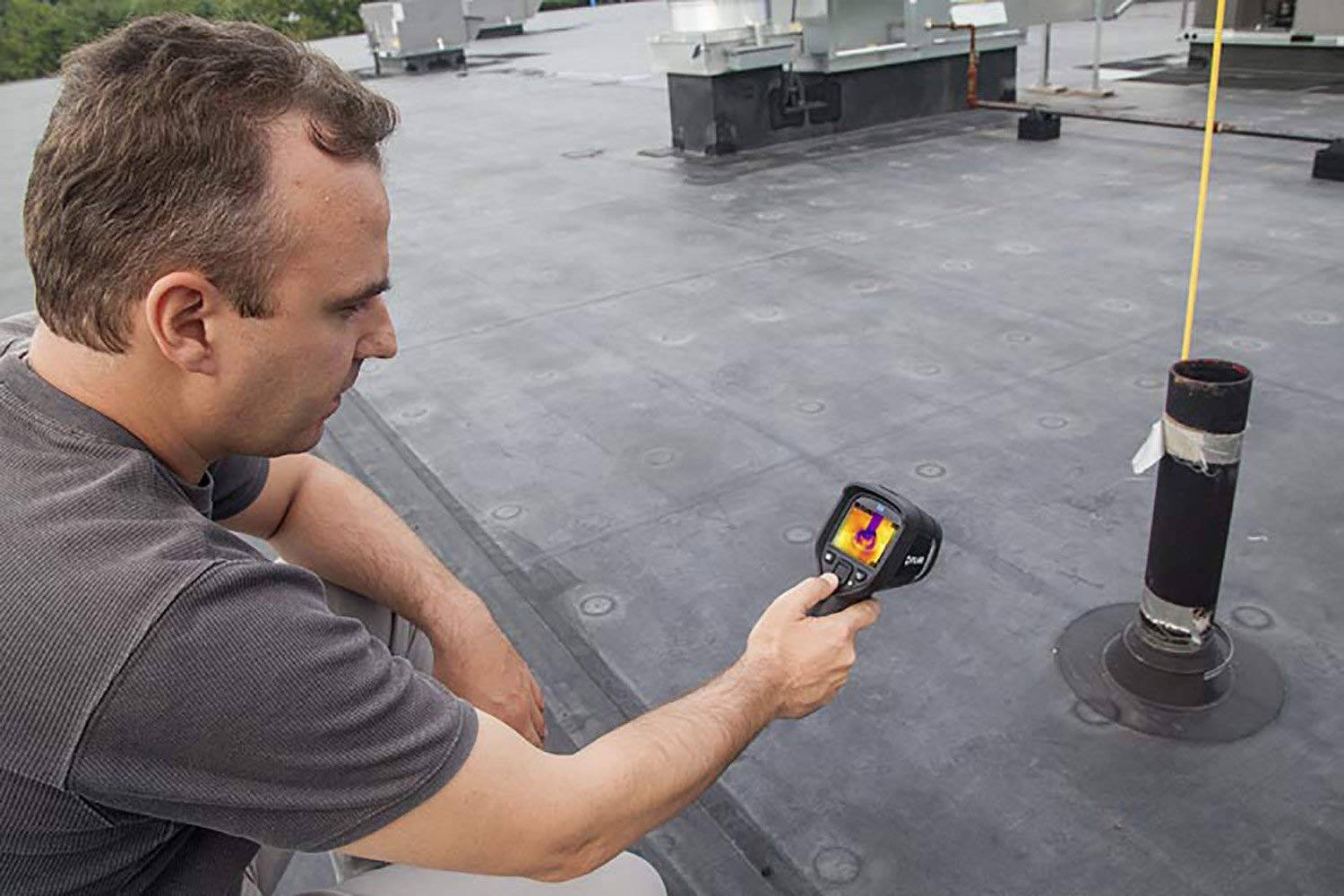 Un homme inspecte un toit à l'aide d'une caméra thermique afin d'identifier d'éventuelles fuites ou problèmes.