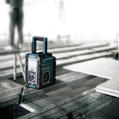 Un poste de radio portable est posé sur une structure métallique. En arrière-plan, des silhouettes floues travaillent sur un chantier de construction.