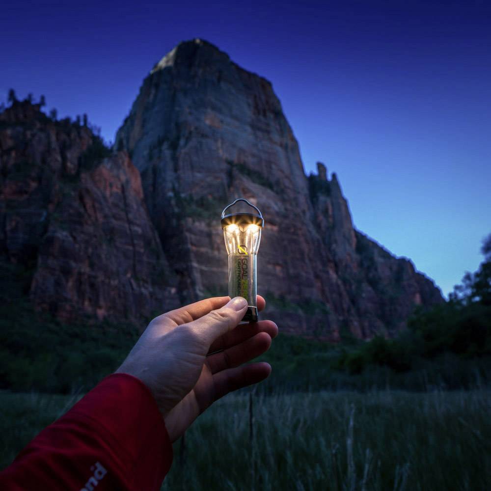 Une personne tient une ampoule lumineuse devant un paysage montagneux au crépuscule, symbolisant la créativité et l'inspiration dans la nature.