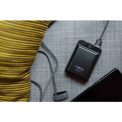 Disque dur externe avec câble USB sur un tissu gris. Un coussin rayé et une surface noire se trouvent en arrière-plan.