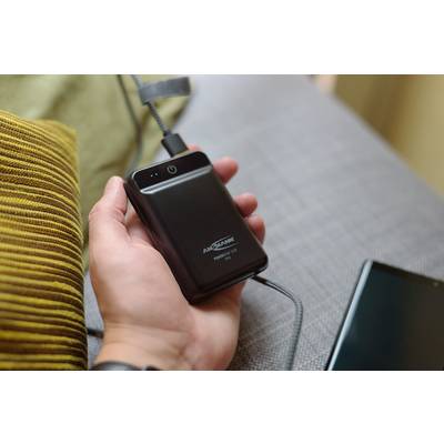 Une personne tient une batterie externe noire portable connectée à un câble de charge. Un canapé est visible en arrière-plan.