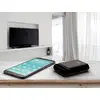 Un smartphone et une batterie externe sont posés sur une table en bois devant un salon moderne avec une télévision en arrière-plan.