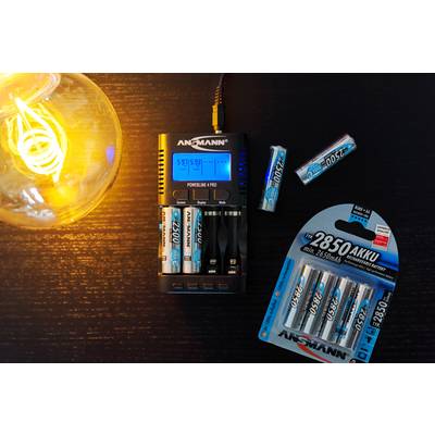 Un chargeur de batteries charge plusieurs batteries. À côté se trouvent des batteries supplémentaires et un emballage. Une ampoule est allumée.
