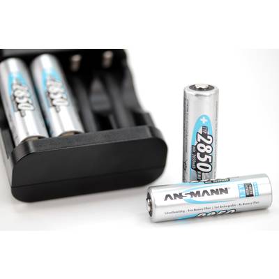Deux piles AA, l'une debout, l'autre couchée, devant un chargeur de batterie. Le nom de marque ANSMANN est visible.