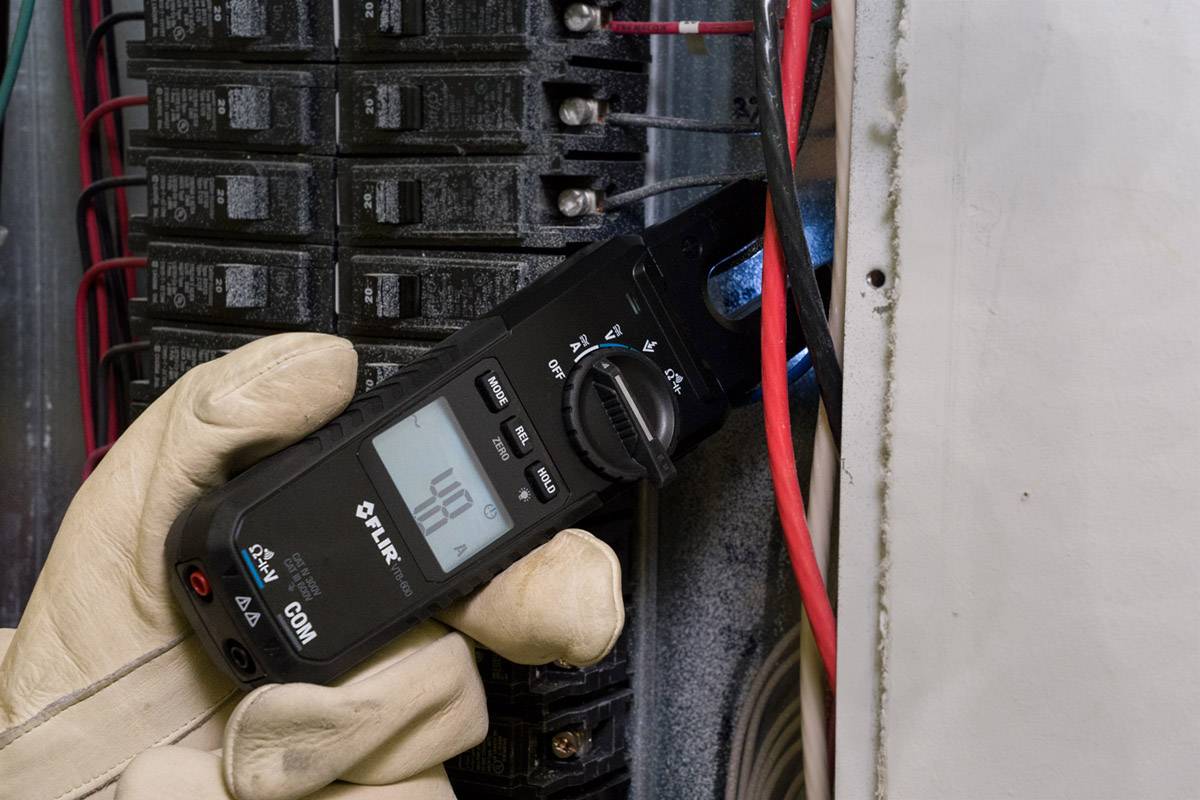 Un électricien utilise un multimètre numérique pour mesurer la tension dans un tableau électrique. Il porte des gants de protection.
