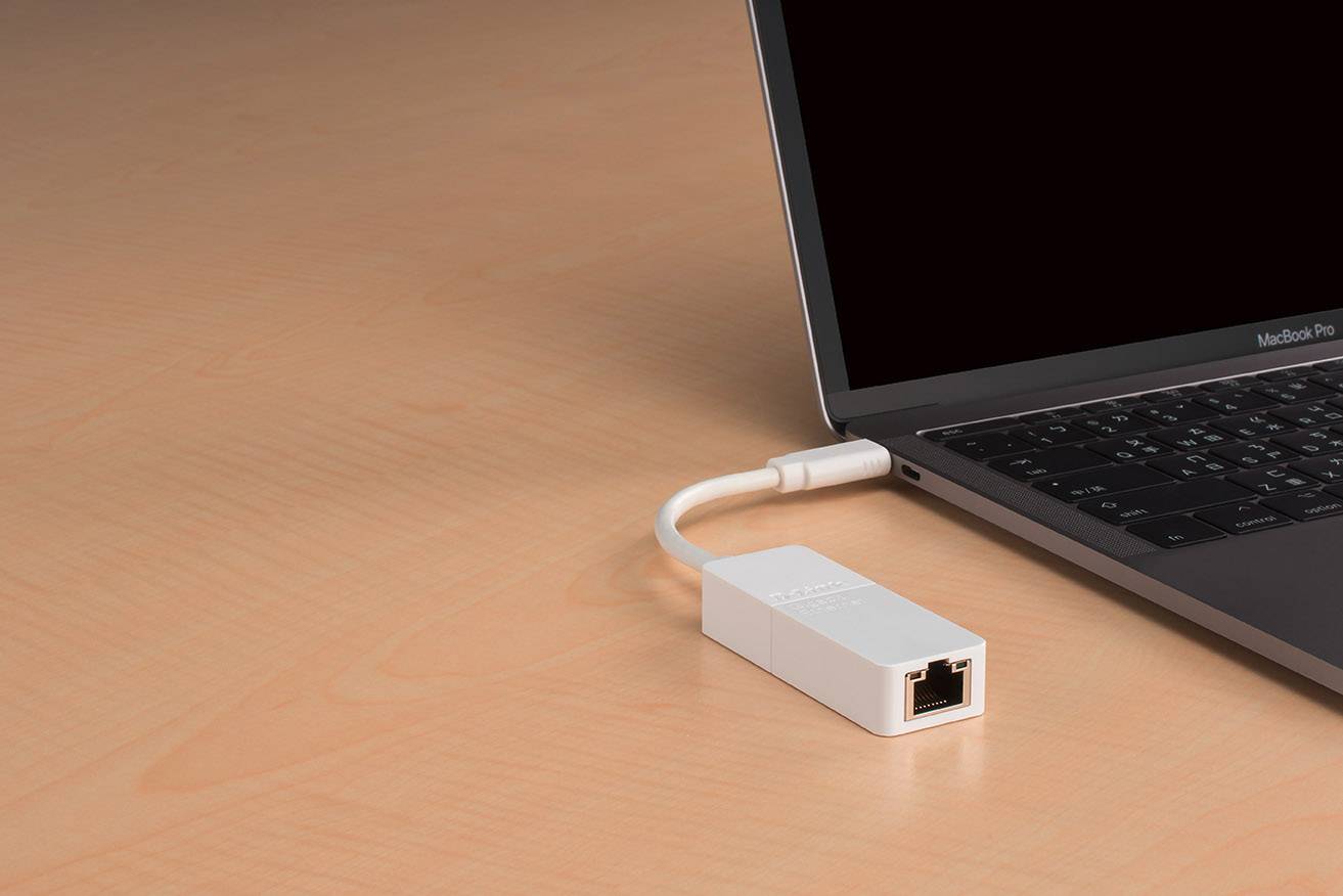 Un adaptateur Ethernet blanc est connecté à un ordinateur portable noir posé sur une table en bois.
