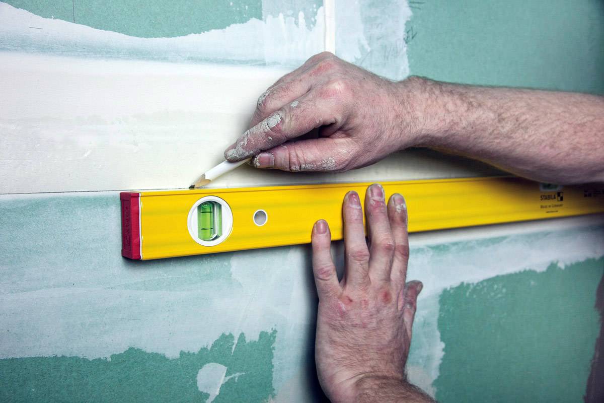 Une personne aligne des carreaux sur un mur à l'aide d'un niveau à bulle. Les mains tiennent le niveau et marquent la ligne.
