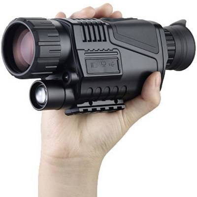 Une main tient un dispositif de vision nocturne avec un objectif et un oculaire. L'appareil est noir et compact, adapté aux observations nocturnes.