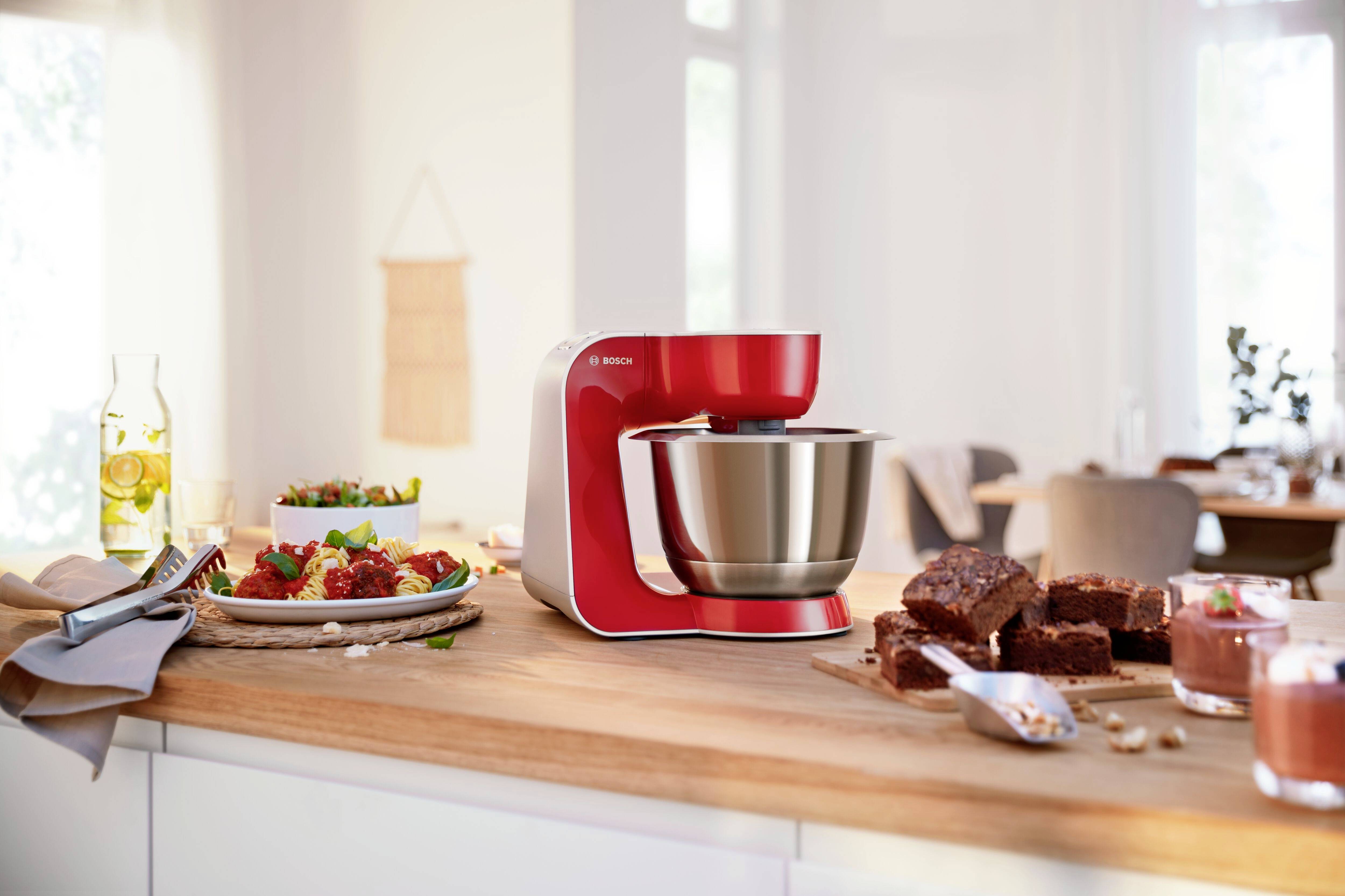 Une machine de cuisine rouge sur un plan de travail à côté d'un plat de brownies et d'un verre de dessert. Cuisine floue en arrière-plan.