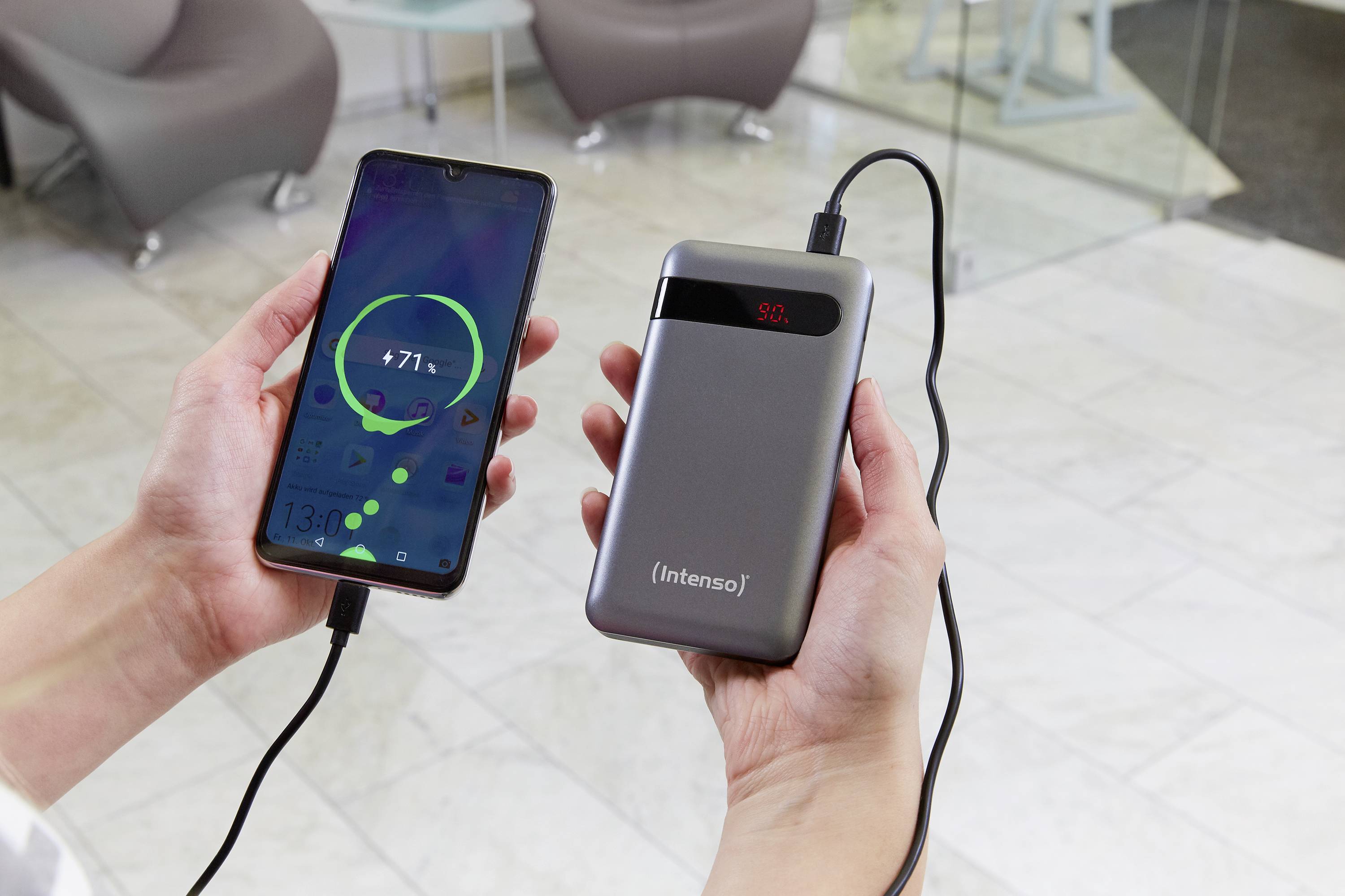 Une main tient un smartphone avec un indicateur de charge, connecté à une batterie externe portable dans l'autre main. La batterie affiche 50%.