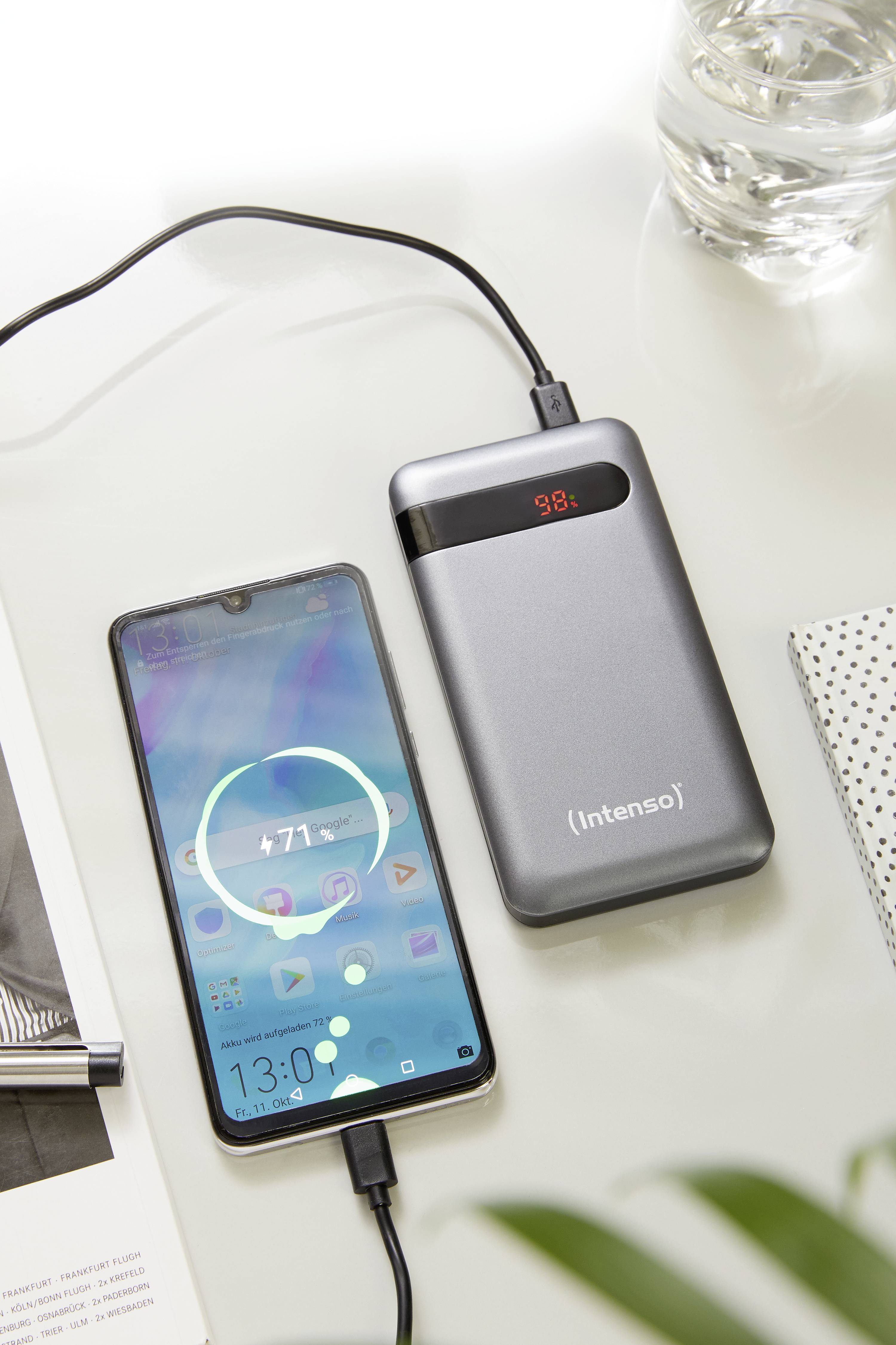 Un smartphone est en train de charger avec une batterie externe argentée de 'Intenso'. L'écran du téléphone affiche le processus de charge.