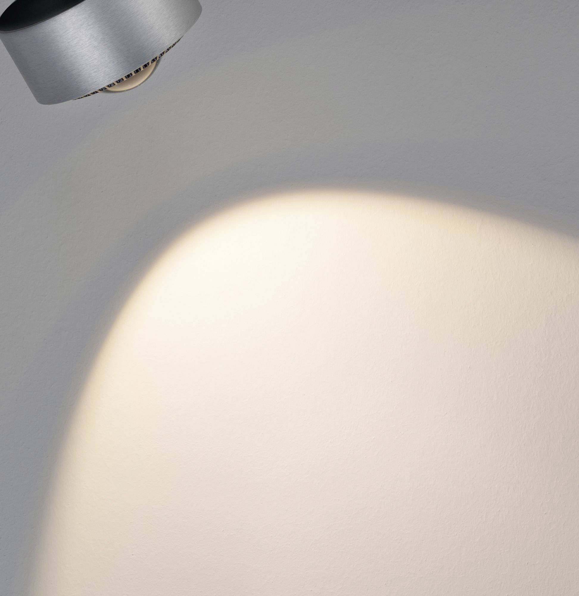 Un applique murale projette une lumière chaude et focalisée sur un mur blanc, créant ainsi une zone lumineuse.