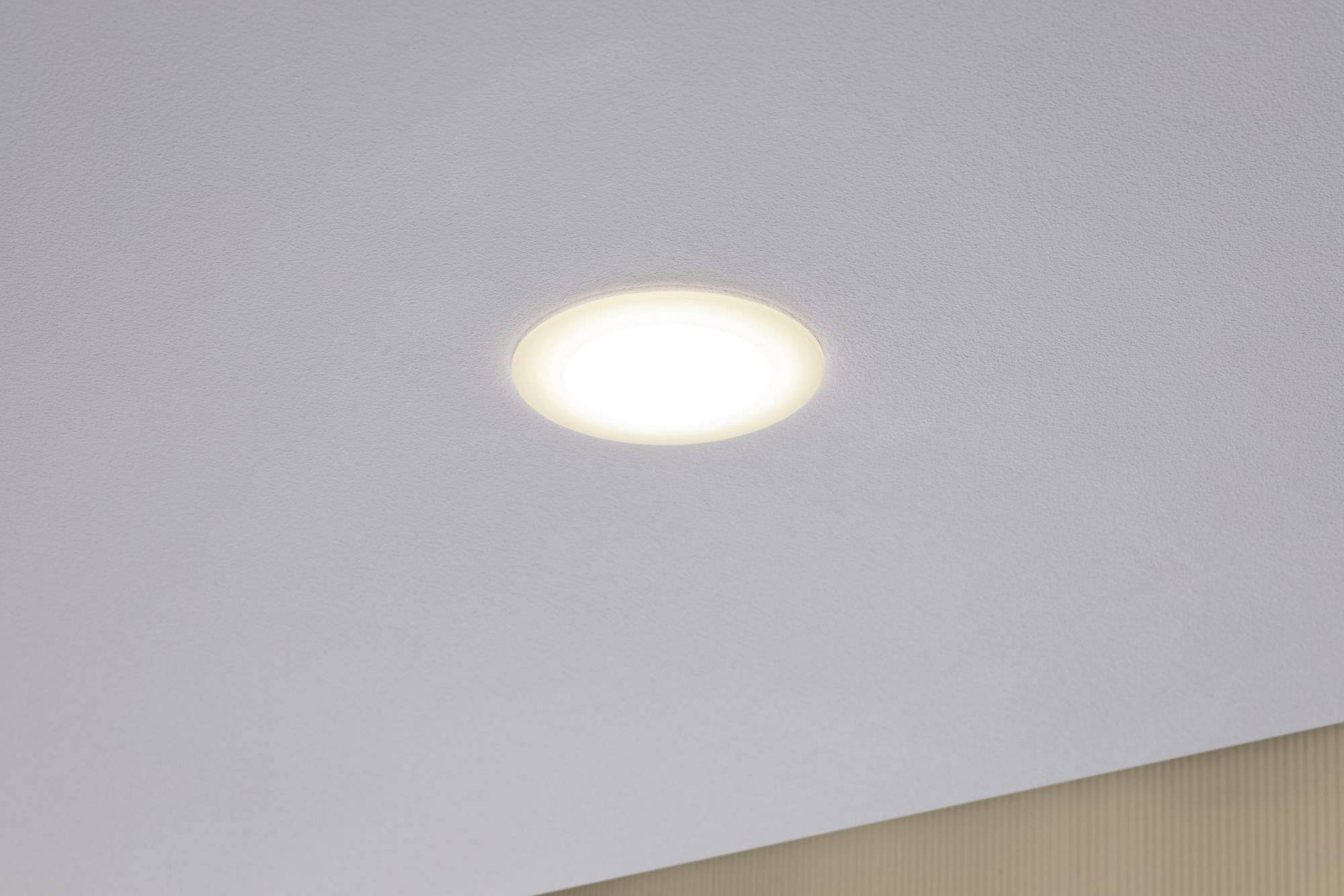Un luminaire LED encastré rond émettant une lumière blanc chaud, sur une surface grise structurée.