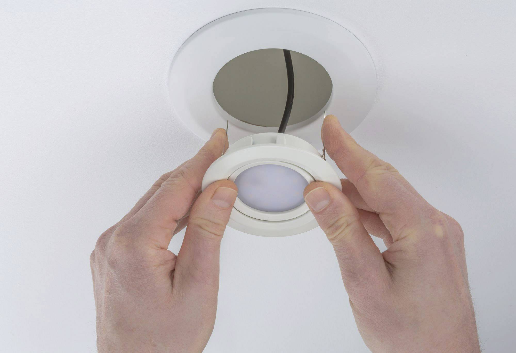 Deux mains installent un luminaire LED rond dans un support de plafond.