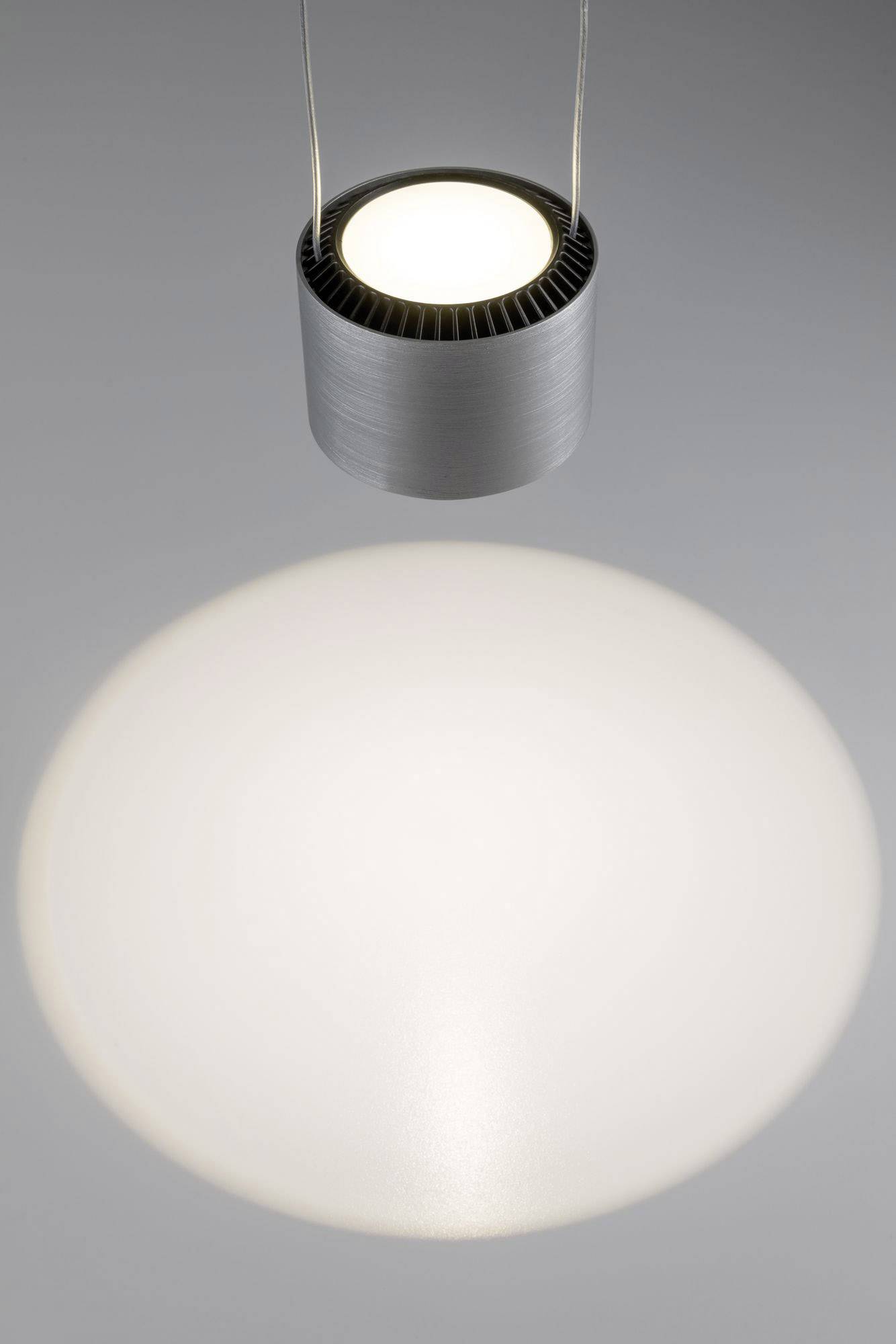 Une suspension cylindrique en métal illumine de haut en bas et crée un halo lumineux circulaire sur la surface grise.