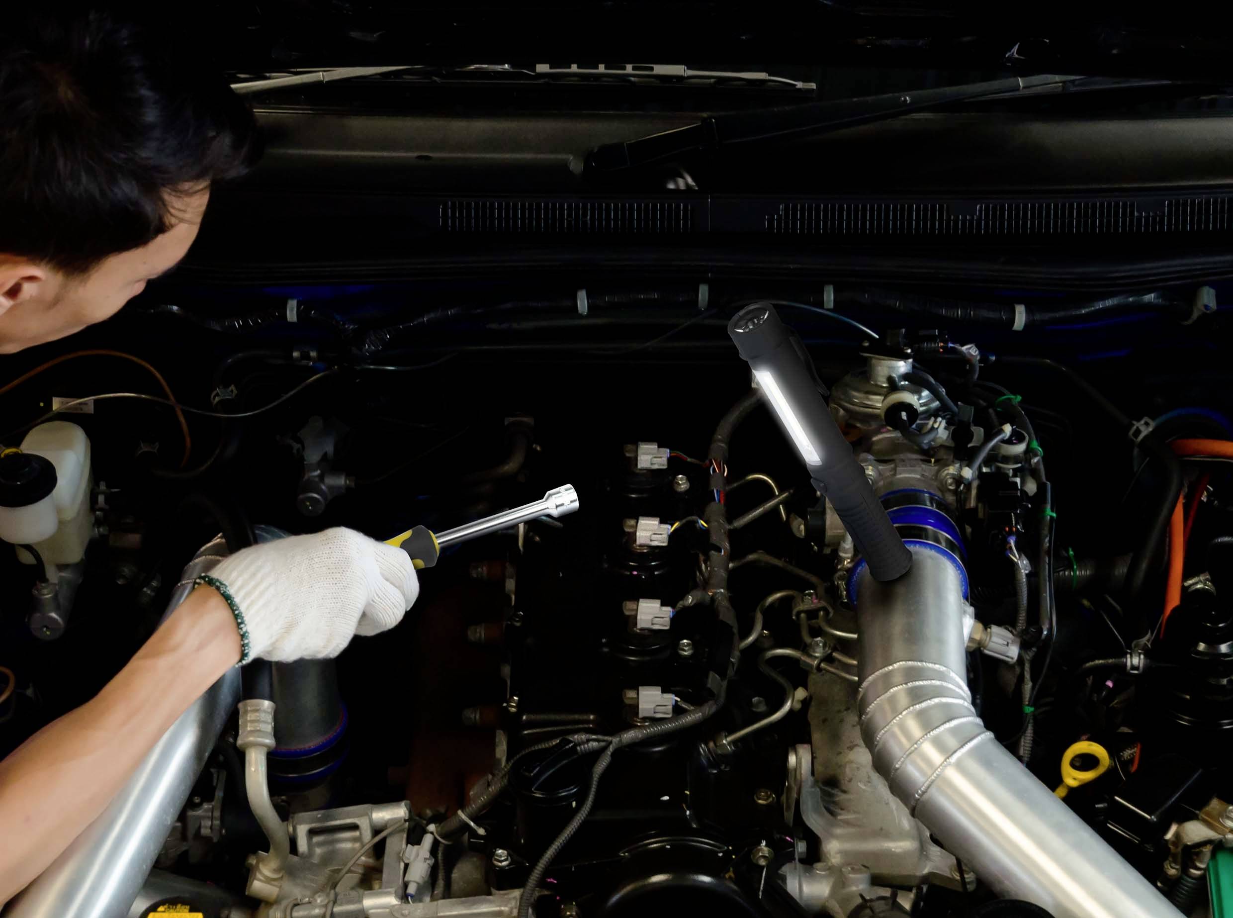 Une personne répare le moteur d'une voiture avec une clé à molette, vue de dessus. Le focus est mis sur les composants du moteur et l'outil.