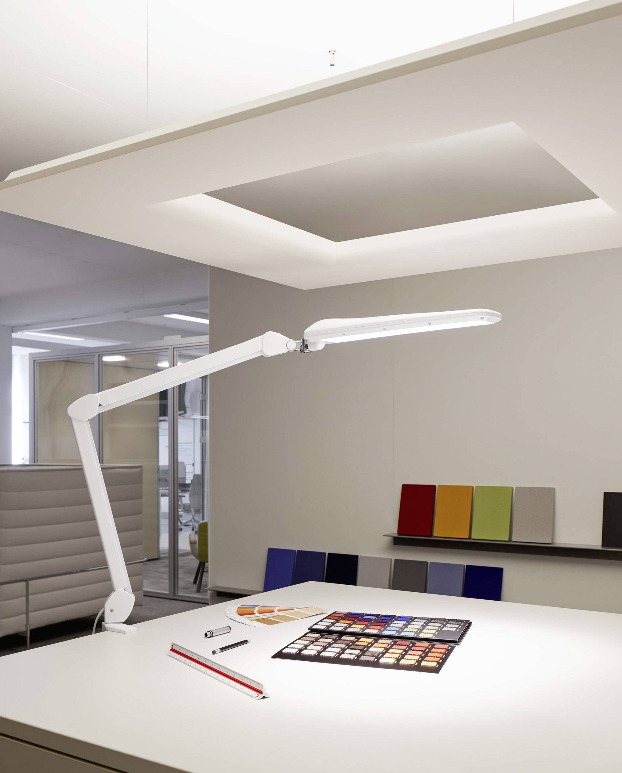 Un bureau moderne avec une lampe de bureau blanche, des nuanciers et des accessoires de design sur la table ; intérieur minimaliste.