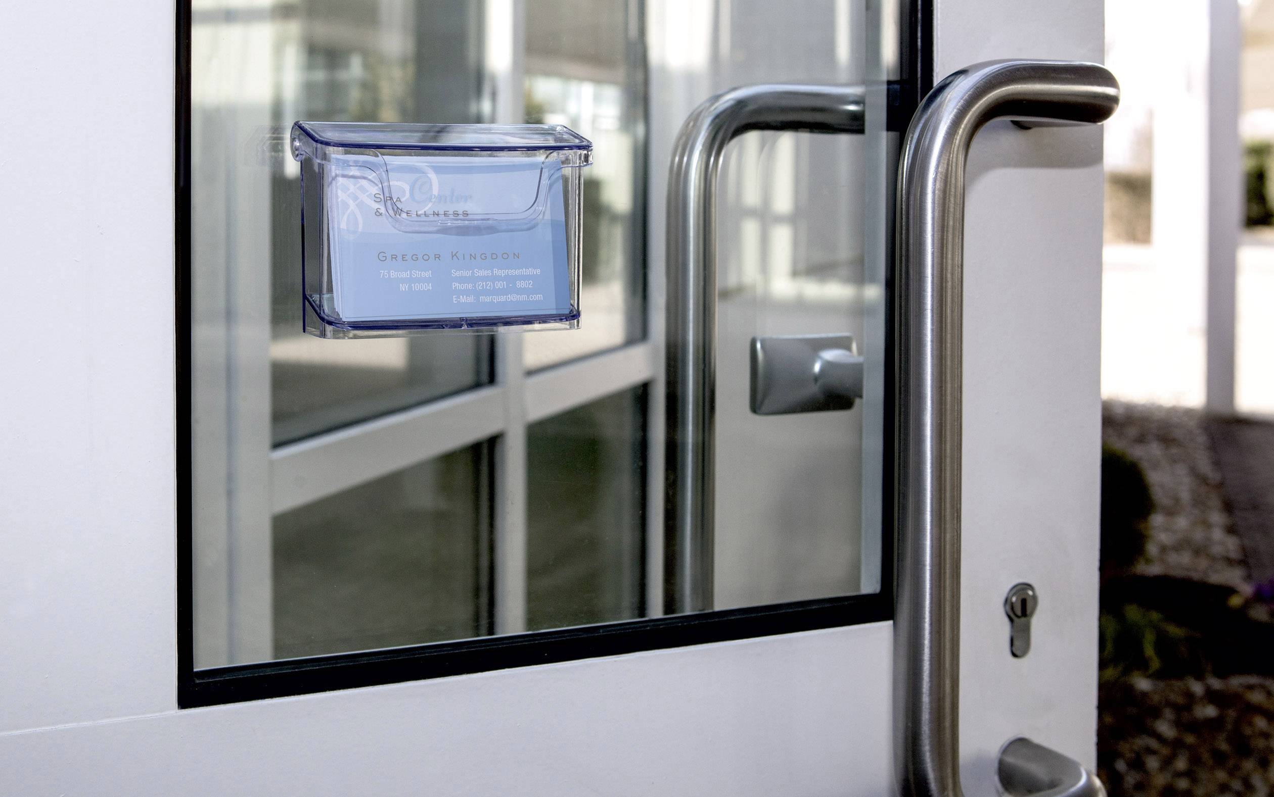 Porte en verre avec une poignée en métal, à côté de laquelle se trouve une vitre sur laquelle est apposé un bouclier bleu affichant des informations de contact.