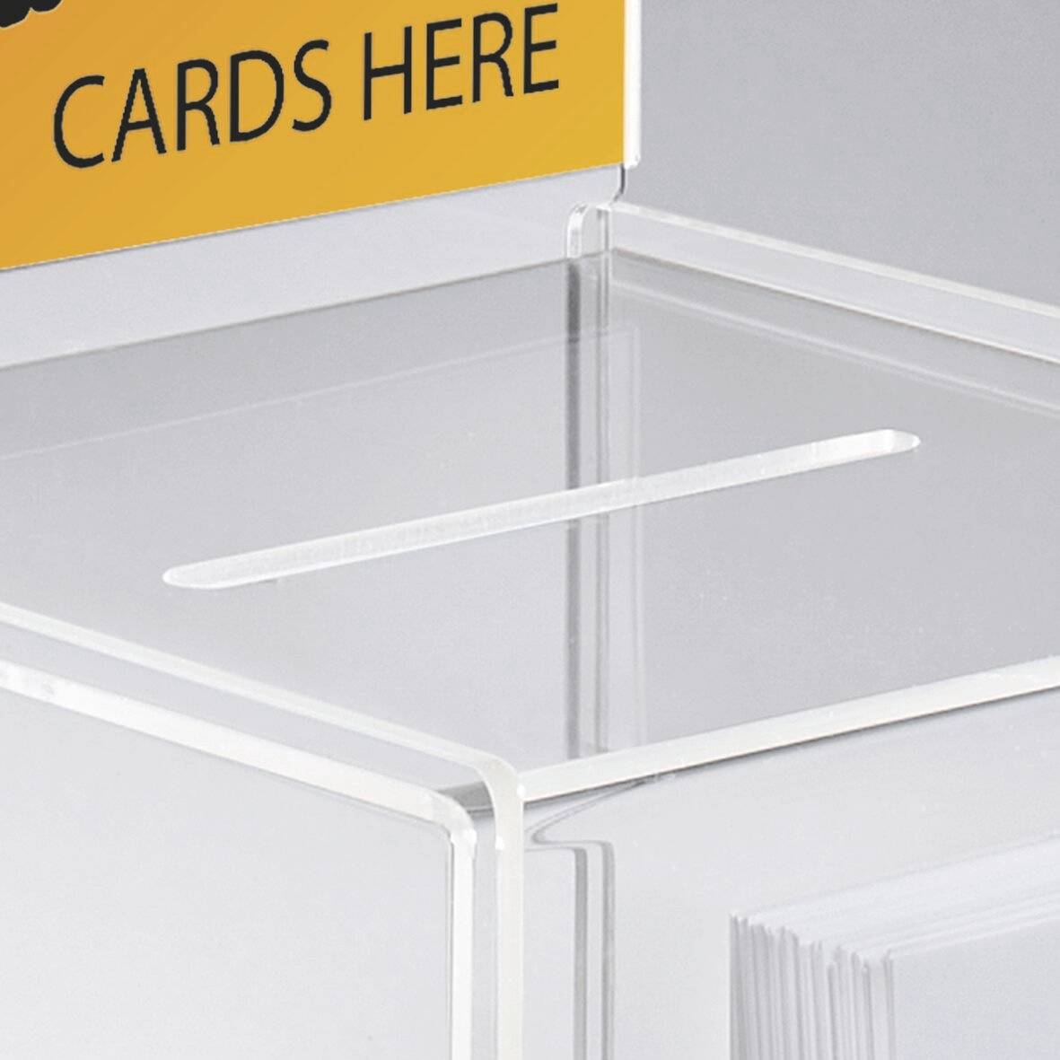 Une boîte transparente avec une fente sur le dessus pour y déposer des cartes, étiquetée « CARTES ICI » sur un panneau orange attaché.