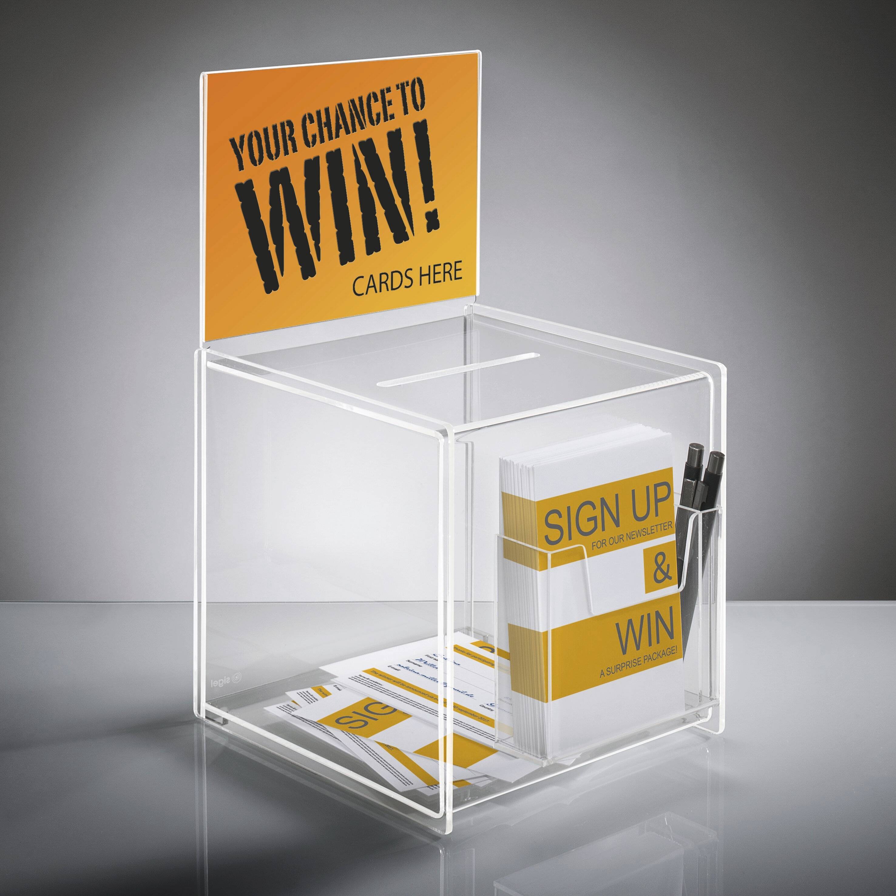 Une boîte de participation transparente avec un panneau au-dessus indiquant « Votre Chance de Gagner ! Cartes ici. » Comprend des cartes d'inscription et un stylo.