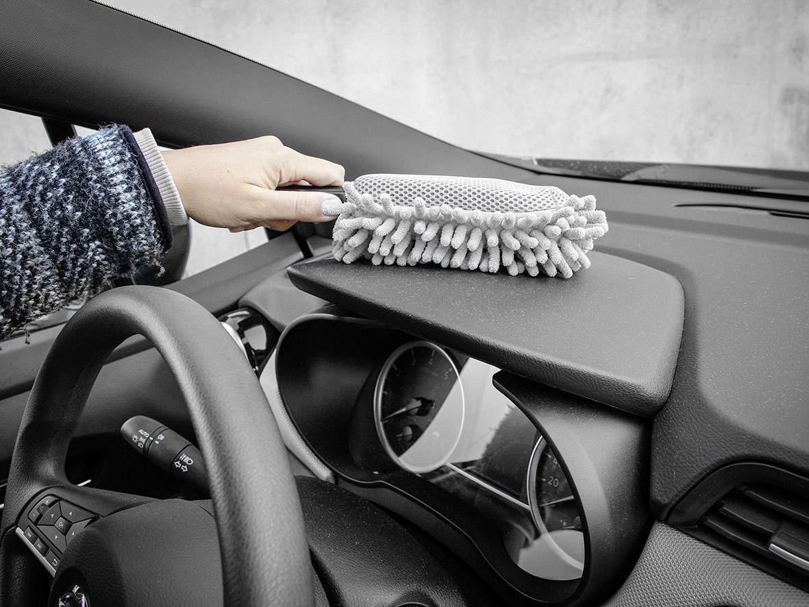 Une personne essuie le tableau de bord d'une voiture avec un chiffon en microfibre gris. L'intérieur de la voiture est visible.