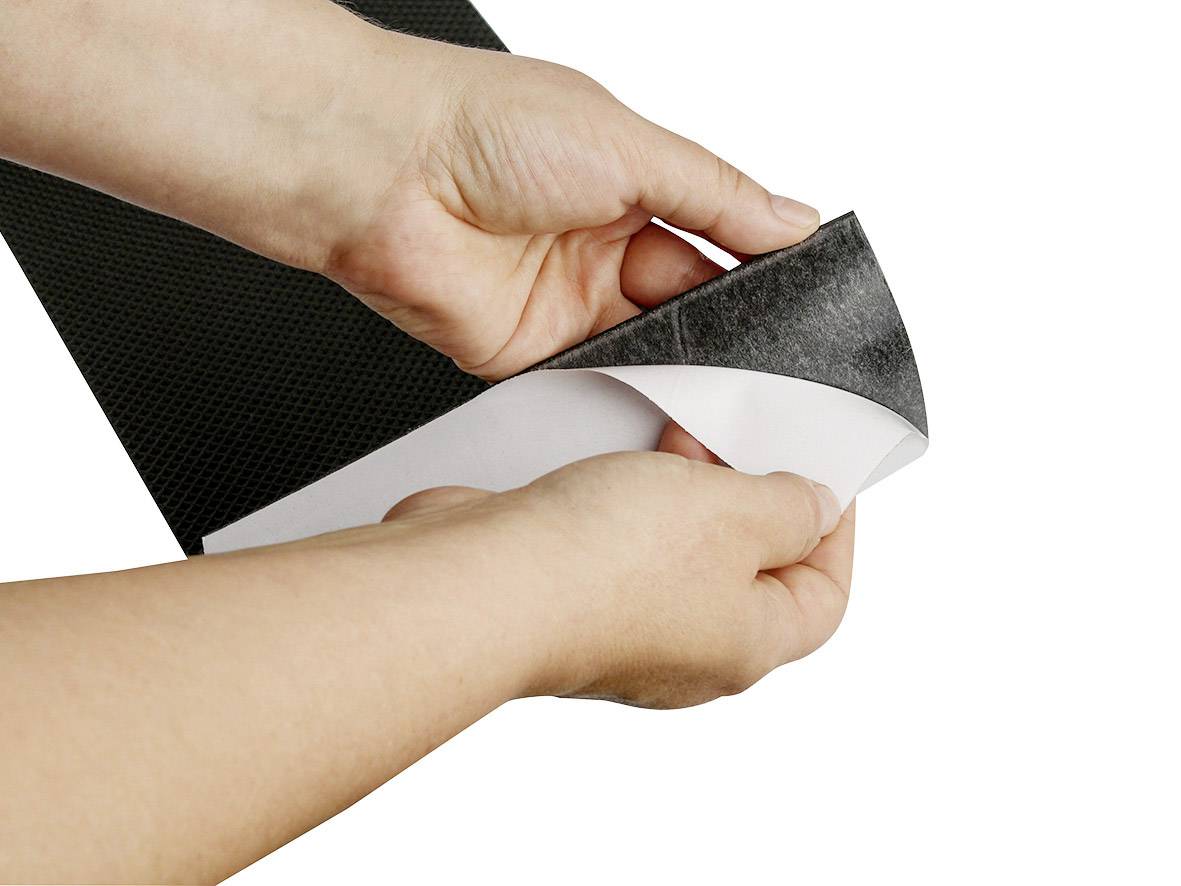 Des mains retirent la couche de protection d'une bande adhésive noire afin d'exposer sa surface collante.