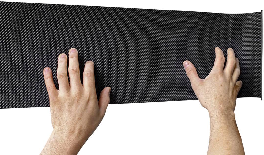 Deux mains tiennent un matériau noir rectangulaire à surface structurée, probablement un tapis ou une plaque.