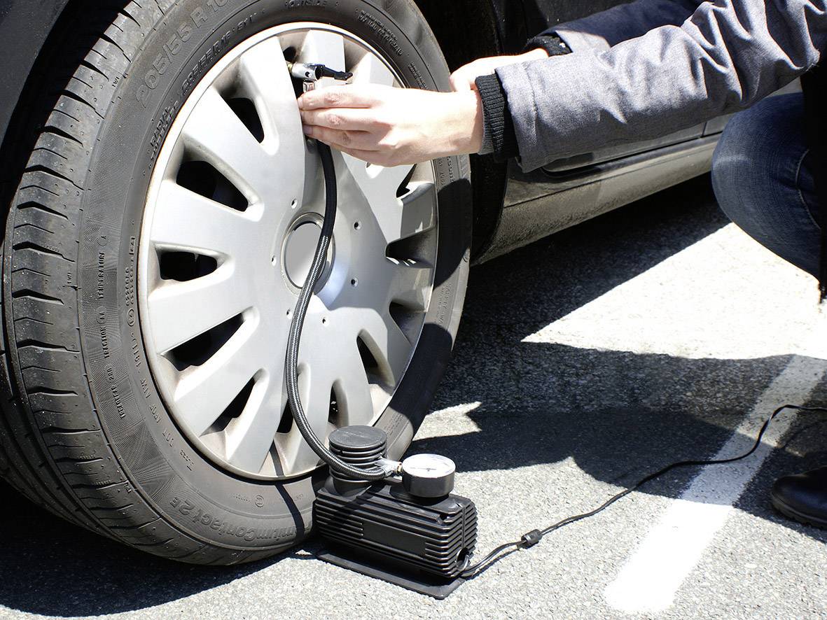 Une personne gonfle un pneu de voiture à l'aide d'un compresseur portable posé au sol. Le compresseur est connecté à la valve du pneu.