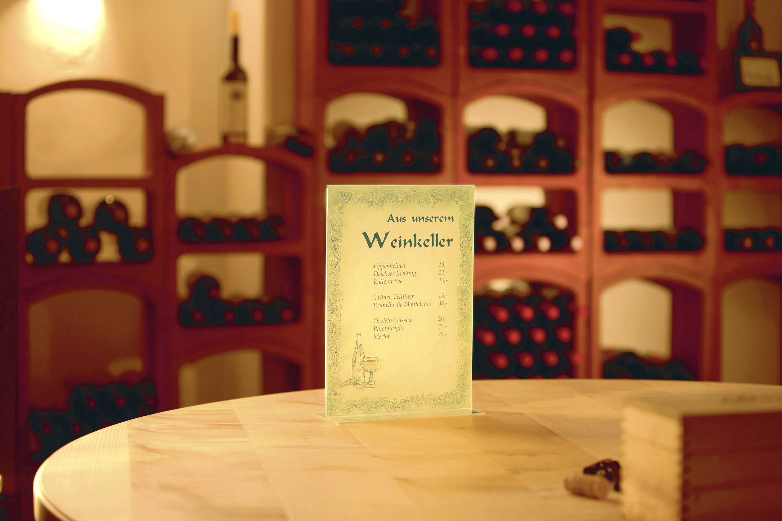 Un menu est posé sur une table dans une cave à vin. À l'arrière-plan, de nombreuses bouteilles de vin sont rangées sur des étagères en bois.