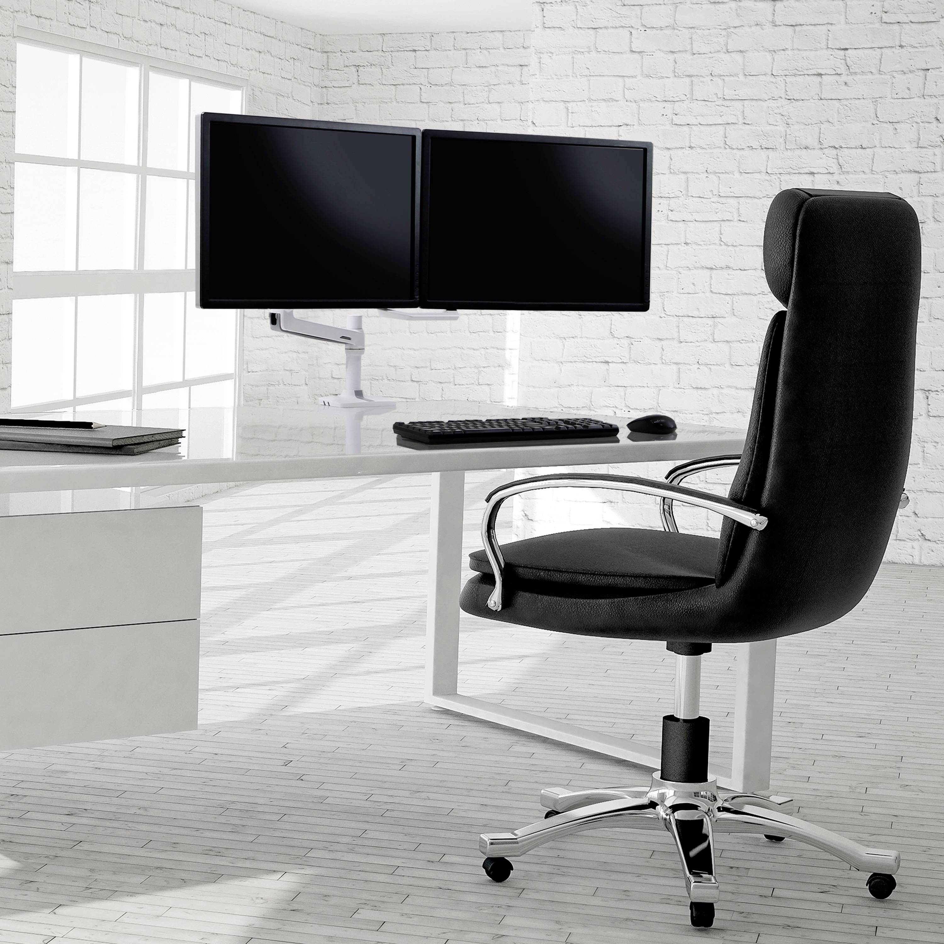 Une chaise de bureau moderne est placée devant un bureau blanc équipé de deux écrans, d'un clavier et d'une souris dans une pièce lumineuse.