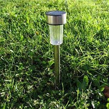 Lampe de jardin solaire, encastrée dans l'herbe verte, avec une tige métallique et un abat-jour transparent, à la lumière du jour.