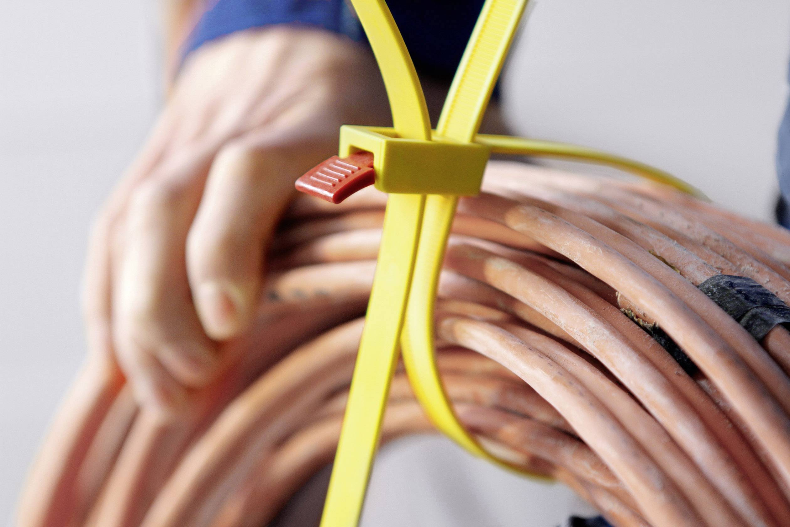 Une main tient un faisceau de câbles orange, attaché avec un serre-câble jaune.