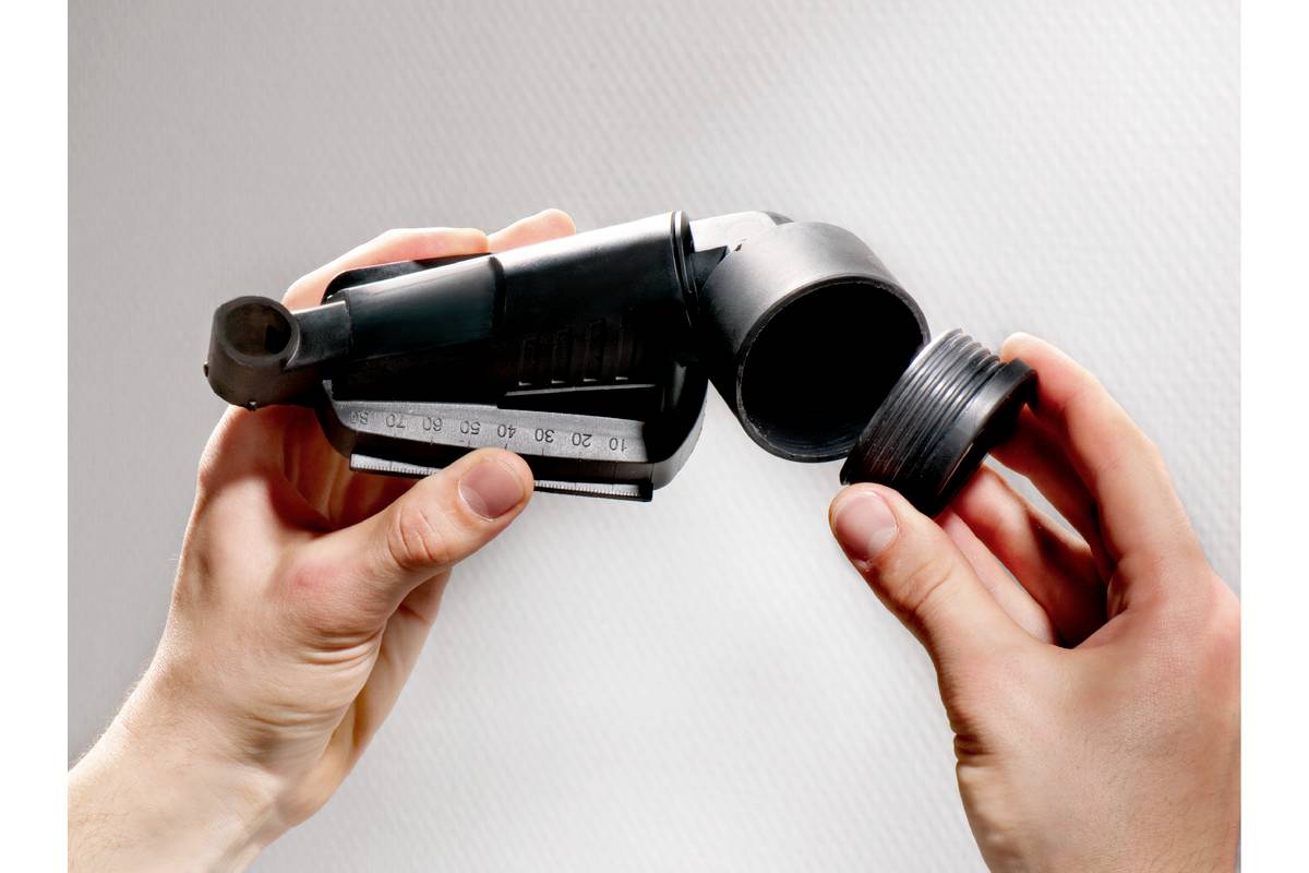 Une personne tient un embout d'aspirateur noir avec un capuchon amovible. L'embout présente un petit récipient doseur.