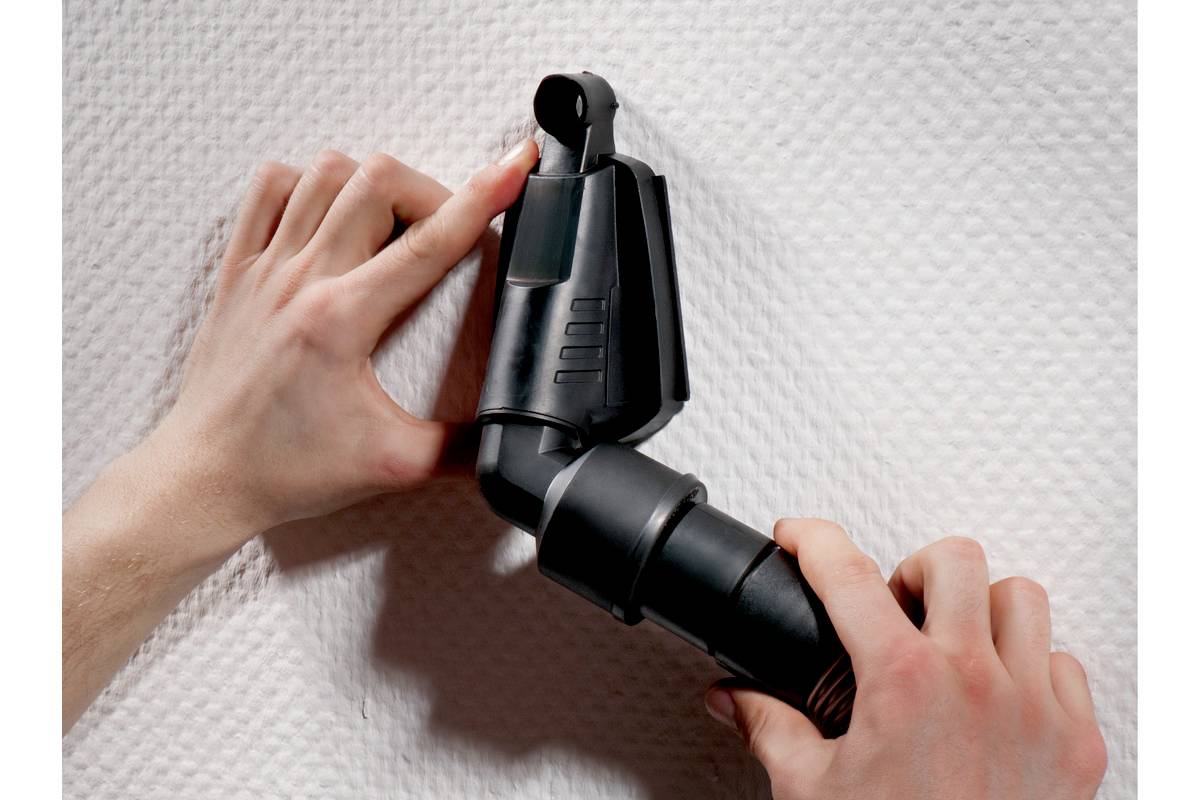 Une personne fixe un dispositif noir sur une surface blanche texturée à l'aide de ses deux mains.