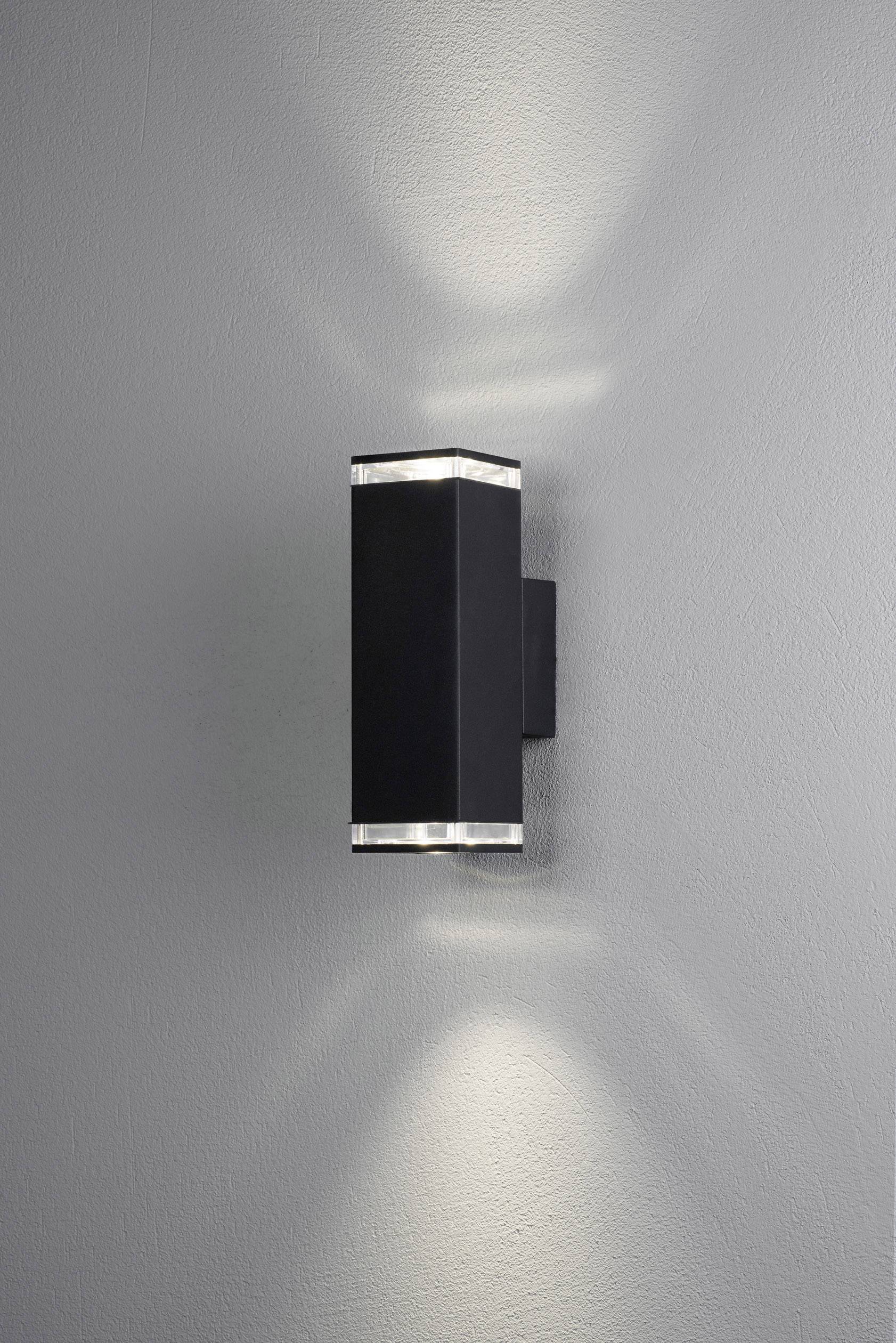 Applique murale rectangulaire noire sur un mur gris, projetant de la lumière vers le haut et vers le bas, créant des cônes de lumière doux.