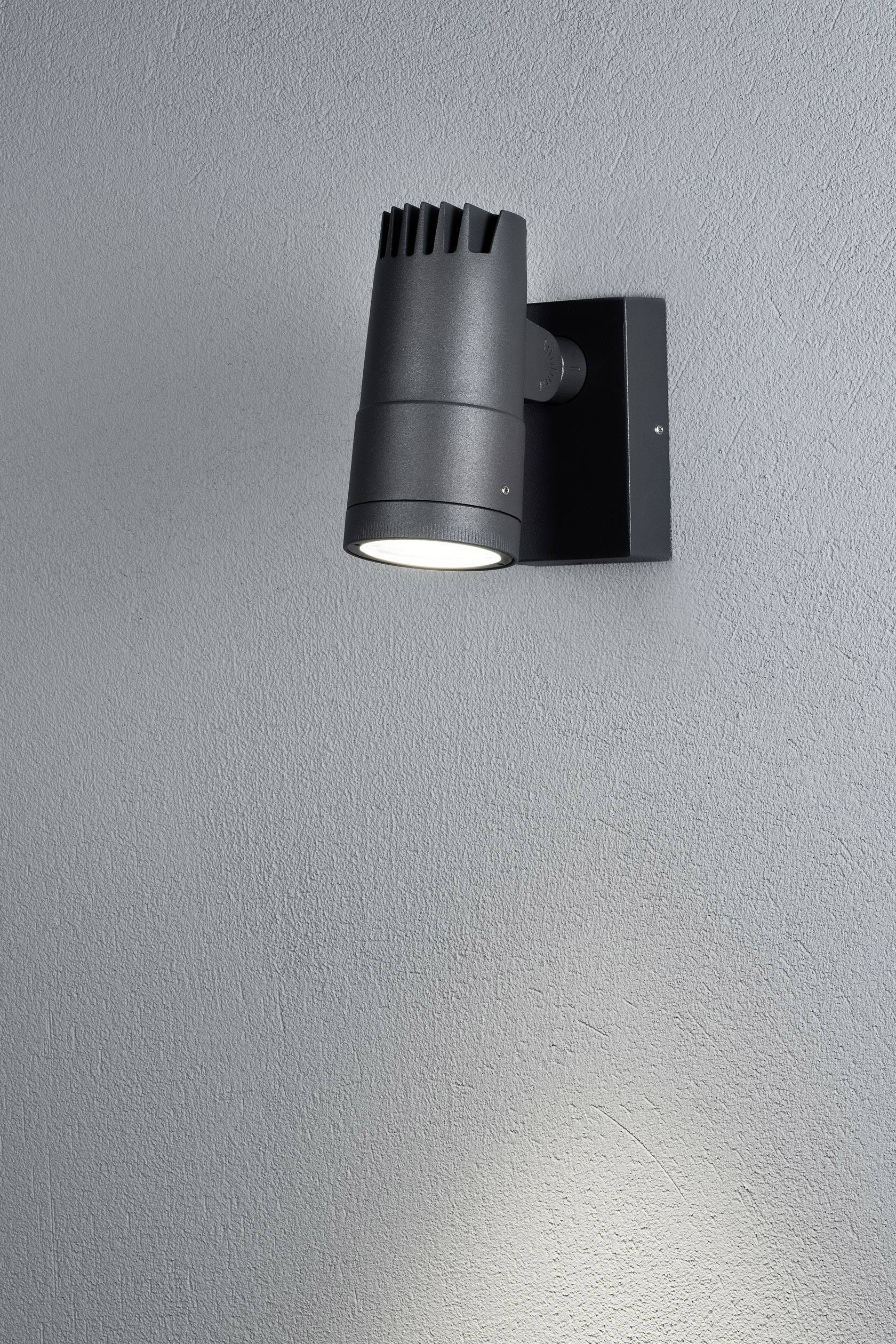 Lampe spot noir fixée au mur, projetant un faisceau lumineux étroit vers le bas et illuminant la paroi.