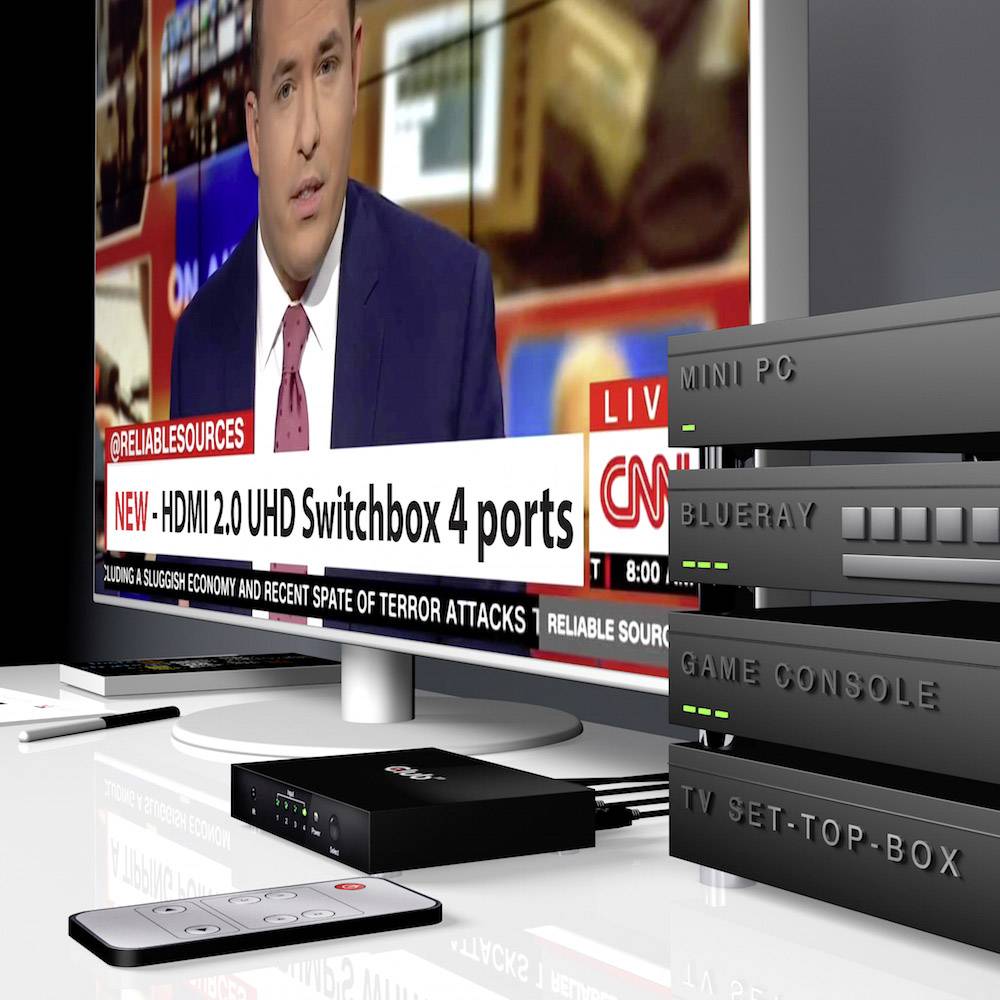 Un présentateur de nouvelles dans un studio ; à gauche, le texte 'Mini PC BluRay Game Console TV Set-Top-Box' est situé à côté d'une pile d'appareils.