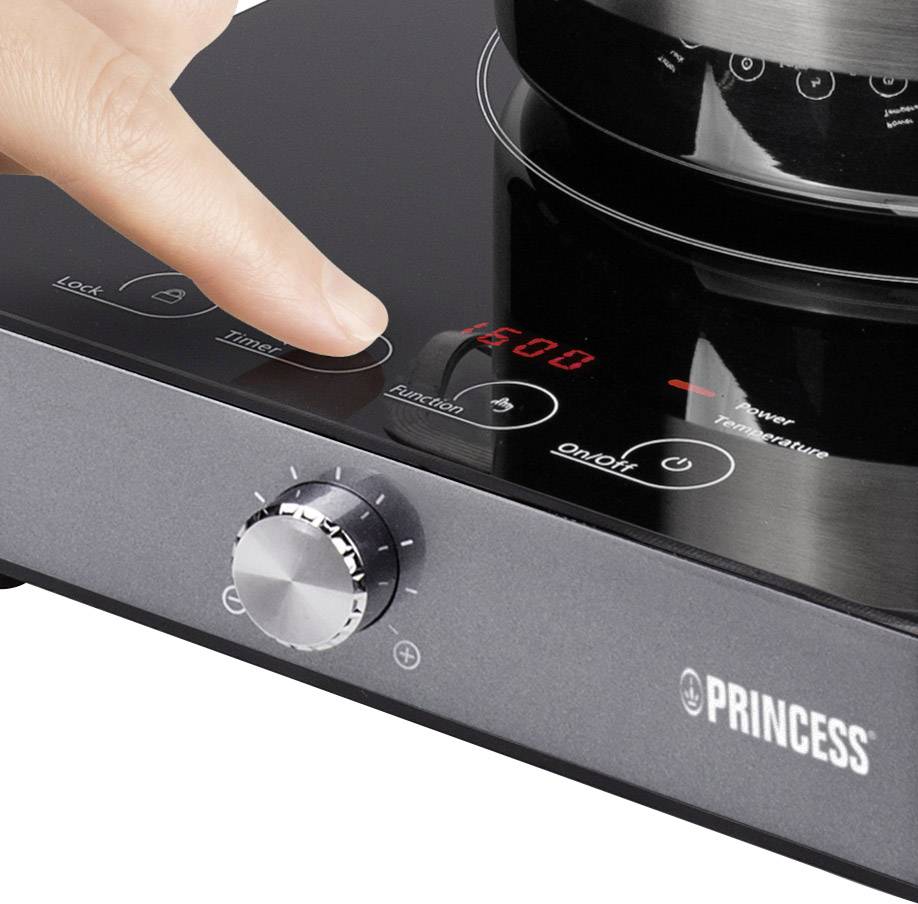 Un doigt touche le panneau de commande d'une plaque de cuisson à induction noire, réglée sur 1500 watts. Le nom de la marque et le bouton de réglage sont visibles.