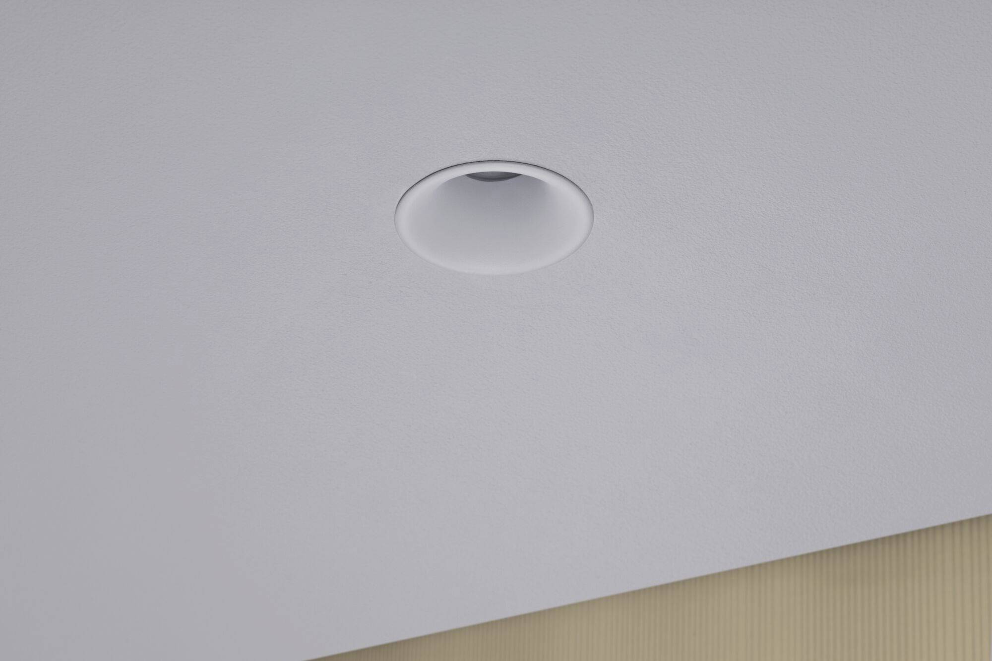 Un luminaire blanc sur un plafond gris, partiellement encadré par une planche de bois, attire le regard vers le haut.