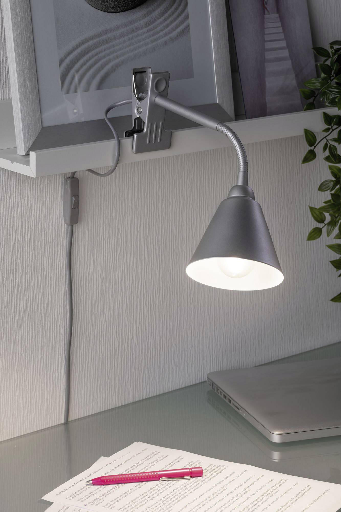 Une lampe de bureau éclaire une table en verre avec des documents et un stylo rouge. Un ordinateur portable est visible en arrière-plan.