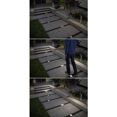 Un chemin piétonnier éclairé devant une maison dans l'obscurité. Une personne remonte le chemin, des lampes carrées marquant le passage.