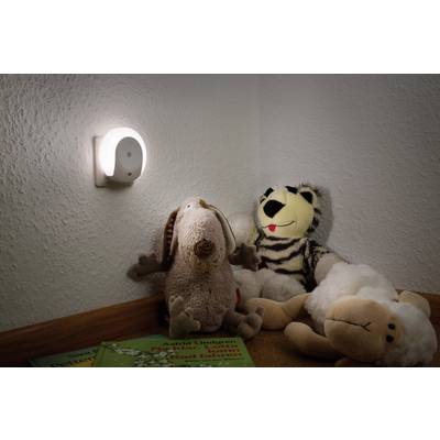 Un coin d'une chambre d'enfant avec une veilleuse accrochée au mur. En dessous, des peluches et des livres pour enfants sont disposés.