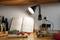 Un livre de recettes est ouvert sous une lampe dans une cuisine. À côté se trouvent des tomates, des carottes, du poireau et des ustensiles de cuisine.